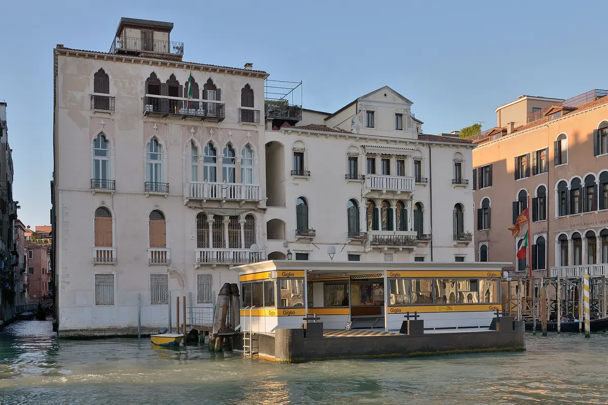 The yellow and white Giglio vaporetto stop floating on the Grand Canal in front of two palazzi